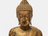 a gold statue of a buddha sitting on a white surface