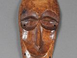un vieux masque en bois posé sur une surface grise
