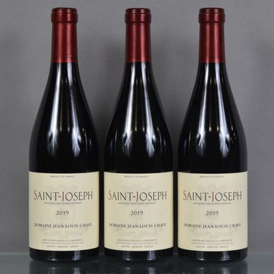 trois bouteilles de vin sont posées sur une table devant un fond gris