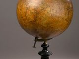 un vieux globe terrestre posé sur un socle, sur fond gris
