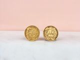 a pair of gold coin stud earrings sitting on top of a marble counter