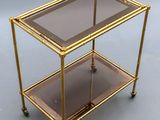 a gold metal and glass bar cart with two shelves on wheels
