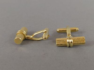 une paire de boutons de manchette en or posés sur une surface grise