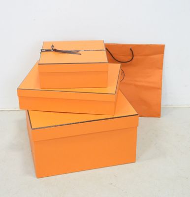trois boîtes orange empilées les unes sur les autres, avec un sac en papier kraft