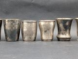 six silver shot glasses lined up in a row on a table