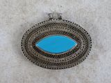a silver and turquoise stone broochle on a white background