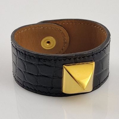 bracelet à manchette en cuir orné de clous pyramidaux dorés sur un fond blanc