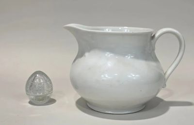 a white pitcher sitting next to an egg on a table