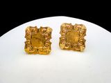 une paire de boucles d'oreilles en or posée sur une assiette blanche avec un fond noir