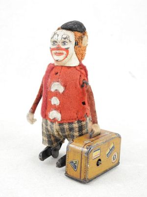 un petit clown en peluche avec une valise, posé sur une surface blanche