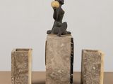 statue of a man sitting on a block with a ball in his mouth
