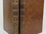 two old books are sitting side by side on a white surface