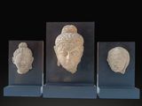 three stone heads of buddhas on display on a black background