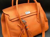 an orange leather handbag with a tassel on a black background