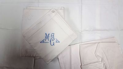 un tissu blanc orné d'un monogramme bleu, à côté d'un pantalon blanc