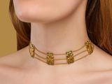 a woman wearing a gold choke necklace with green stones