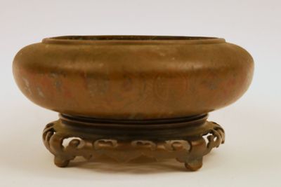 un petit bol en bronze posé sur un socle, sur une surface blanche