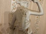 a statue of a woman that is standing in front of a wallpapered wall