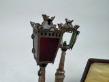 a silver and red clock on a stand next to a box