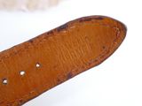 someone is holding a brown leather watch strap with a white shell in the background