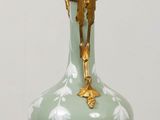 a green vase sitting on a table with a gold base