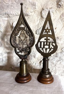 paire de trophées anciens en laiton posés sur des socles en bois, avec un mur en pierre en arrière-plan