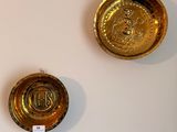 two gold plates on a white wall with a tag attached to them