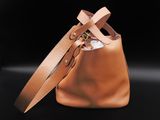 a brown bucket bag with two handles and a strap on a black background