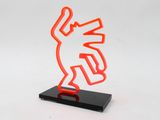 an orange neon sculpture on a black stand with a white background