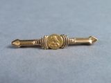 a close up of a gold tie bar with a coin on it