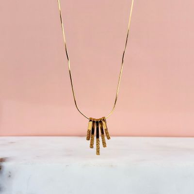 un collier en or auquel sont suspendus cinq lingots d'or, sur fond rose