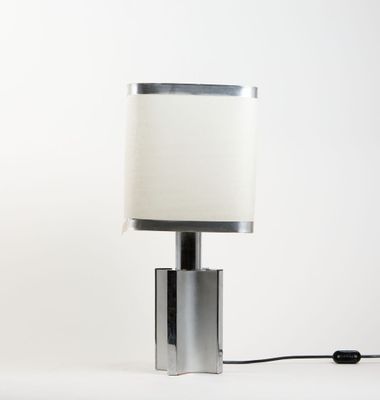 une lampe de table argentée surmontée d'un abat-jour blanc