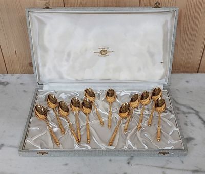 six cuillères en or dans un coffret en argent posé sur une table en marbre