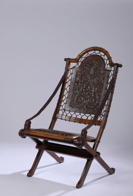 une vieille chaise en bois dont le dossier et l'assise sont sculptés, posée sur une surface blanche