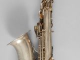 un vieux saxophone argenté muni d'un manche en bois, sur fond gris