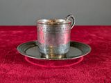 a silver cup and saucer on a red table cloth