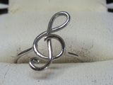 une bague en argent avec une note de sol au centre, posée sur un tissu blanc