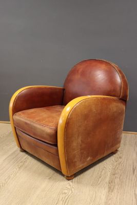une image représentant un fauteuil en cuir marron posé sur un parquet en bois massif