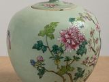a green vase with pink flowers on it sitting on a table