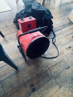 un ventilateur rouge posé par terre à côté d'un sac noir