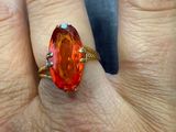 une image représentant la main d'une femme tenant une bague sertie d'une pierre orange