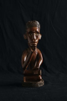 une statue en bois représentant un homme, la main posée sur le menton