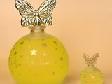 un flacon de parfum orné d'un papillon sur le bouchon, à côté d'un petit flacon de parfum