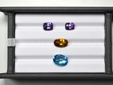 trois pierres précieuses de couleurs différentes dans une boîte noire posée sur une surface blanche