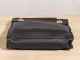 black leather handbag sitting on a wooden table with a white background