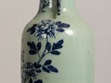 a green vase with blue flowers on it sitting on a table