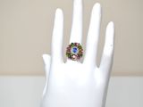 a white hand with a ring on it that has multi colored stones on it