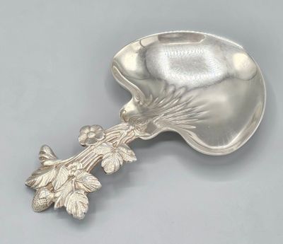 an antique silver spoon with leaves on it on a gray surface