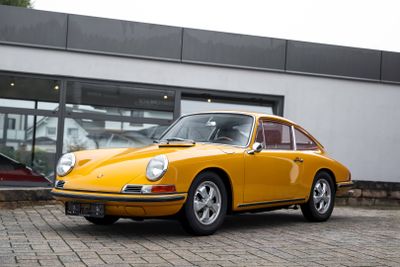 une Porsche 911 jaune garée devant un immeuble, avec une voiture en arrière-plan