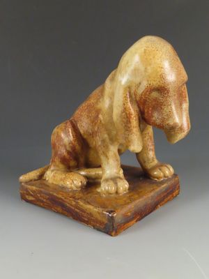 statue d'un chien assis sur un socle en bois, posée sur une surface grise